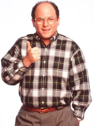 Eine Person posiert mit Daumen hoch, trägt eine Brille und ein kariertes Hemd.