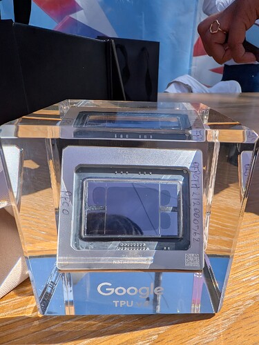 Une vue rapprochée présente une puce Google TPU v4 dans un présentoir transparent, révélant les composants internes complexes et portant le logo Google. (Légendé par l'IA)