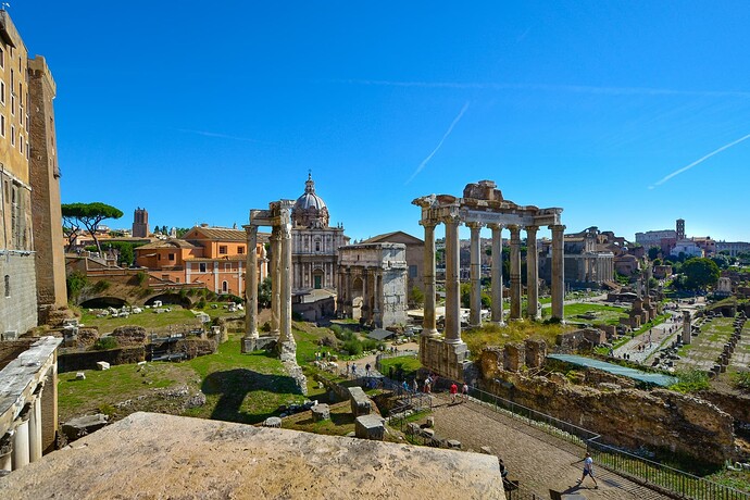 Una vista soleggiata dell'antico Foro Romano, che mostra rovine di edifici storici e colonne contro un cielo azzurro limpido. (Sottotitolato dall'IA)